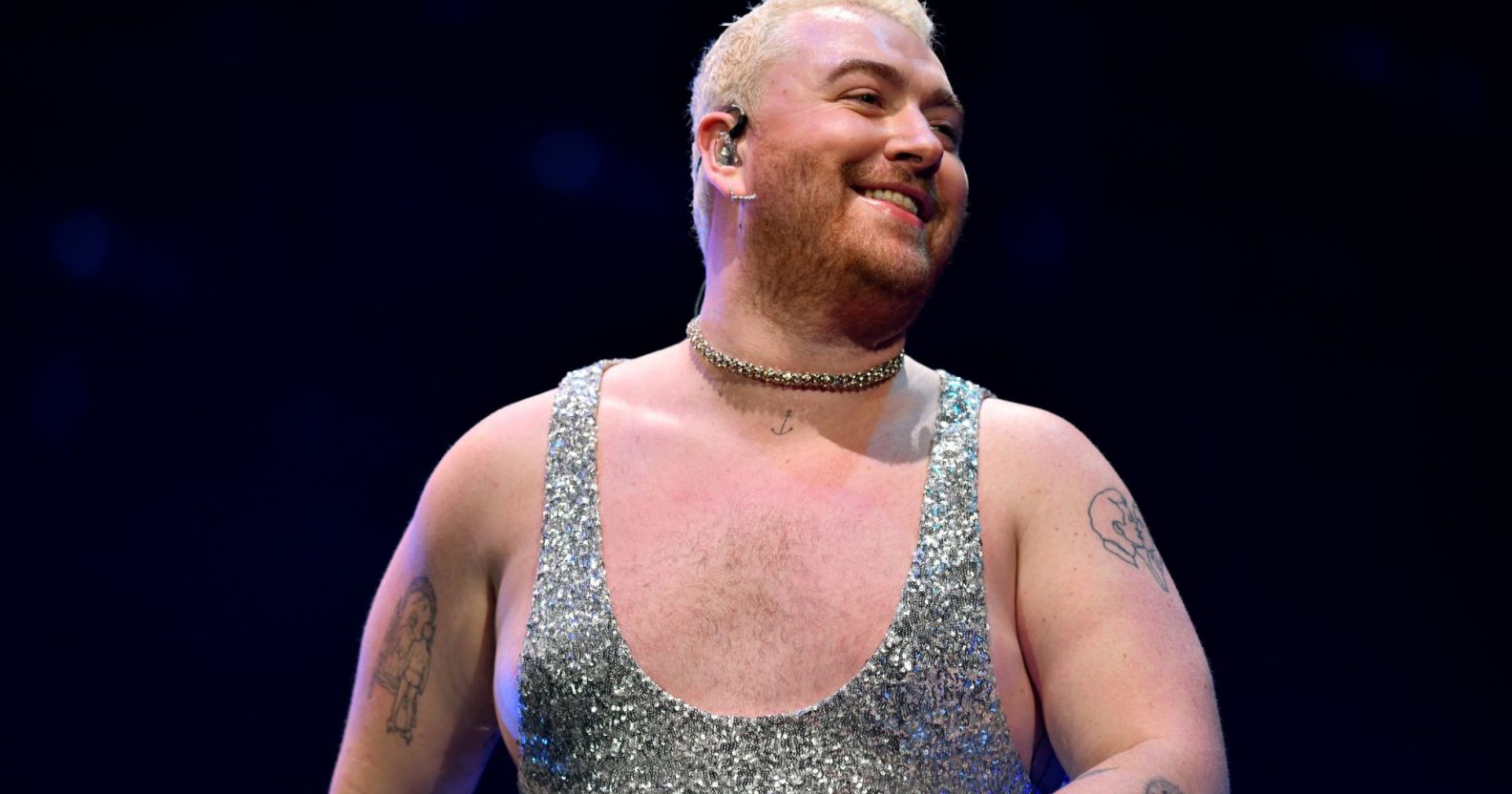 Sam Smith smiling while performing at the 2022 Jingle Bell Ball wearing a silver glittery jumpsuit