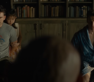 A still from the movie Knock at the Cabin shows two men tied to their chairs in a room with the top half of someone's head looking at them in the foreground of the image