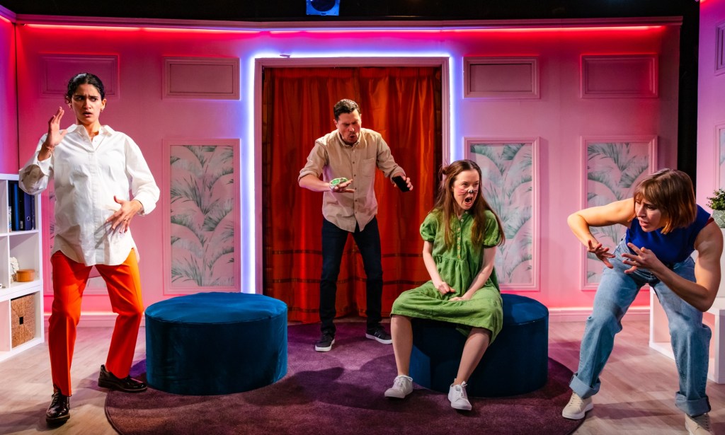 A photo from the play The Boys are Kissing with actors Seyan Sarvan, Philip Correia, Amy McAllister and Eleanor Wyld performing in a bright pink and neon lit living-room style set.