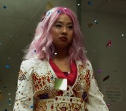 A screenshot from the movie Everything Everywhere All at Once shows actor Stephanie Hsu as character Joy who's dressed in a white and red oriental-style outfit with her hair dyed pink.