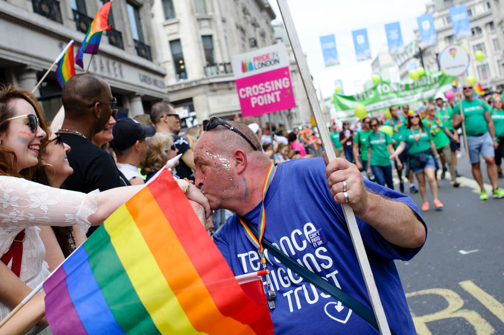 A marcher is seen wearing a Terrence Higgins Trust t-shirt and kissing the hand of a person looking on at a Pride March.