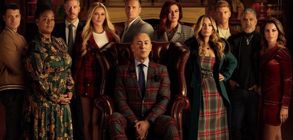 A screenshot from the The Traitors US trailer shows the 10 contestants in a large room standing round actor Alan Cumming who is sat in a big leather chair. (Peacock)