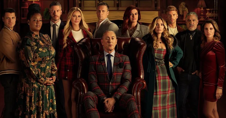 A screenshot from the The Traitors US trailer shows the 10 contestants in a large room standing round actor Alan Cumming who is sat in a big leather chair. (Peacock)