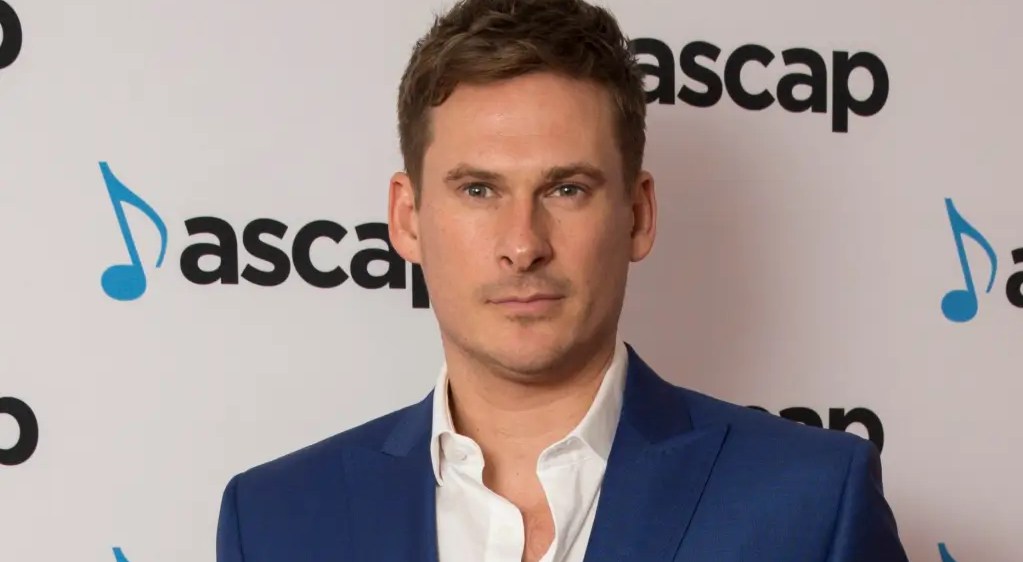 Lee Ryan in a blue suit with white open collar shirt