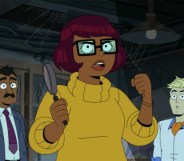 A still from new HBO Max cartoon Velma shows main character Velma Dinkley wearing a yellow sweater and holding magnifying glass in one hand while Fred dressed in white shirt and orange cravat is standing to the right. (HBO Max)