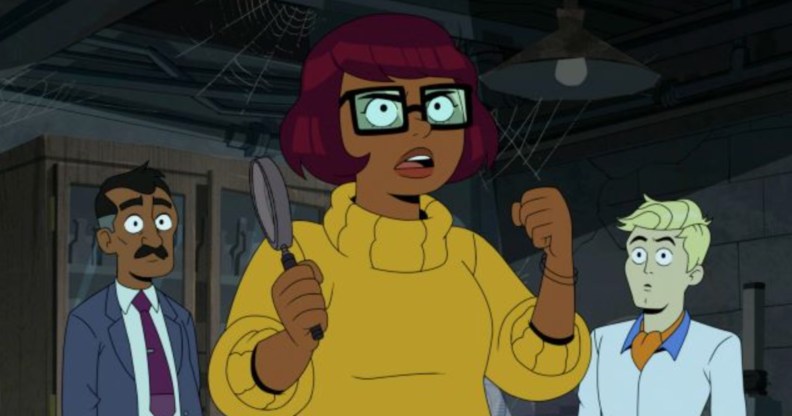 A still from new HBO Max cartoon Velma shows main character Velma Dinkley wearing a yellow sweater and holding magnifying glass in one hand while Fred dressed in white shirt and orange cravat is standing to the right. (HBO Max)