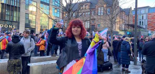 One of the protesters, a white woman with red hair holding a Pride flag, in front of a crowd of others
