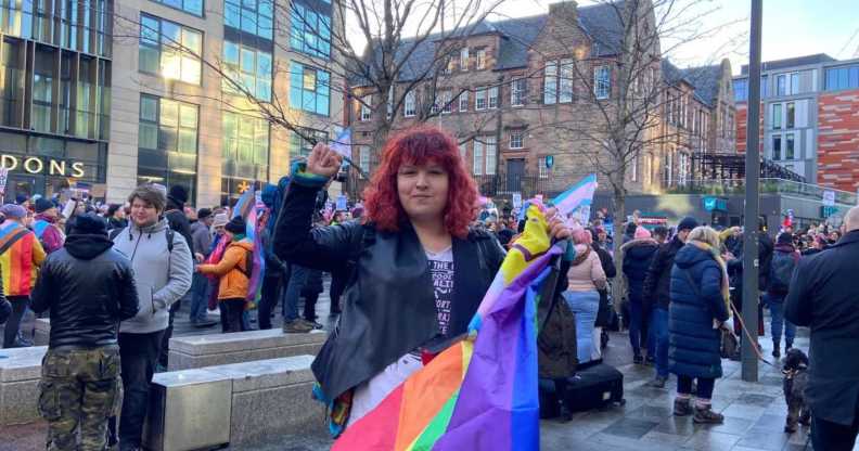 One of the protesters, a white woman with red hair holding a Pride flag, in front of a crowd of others