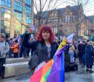 One of the protesters, a white woman with red hair holding a Pride flag, in front of a crowd of others