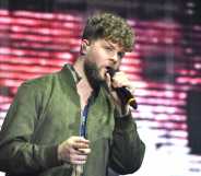 A photo of The Wanted's Jay McGuinness wearing a green top and singing into a microphone while performing on stage