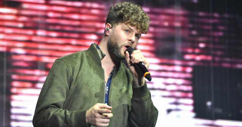 A photo of The Wanted's Jay McGuinness wearing a green top and singing into a microphone while performing on stage