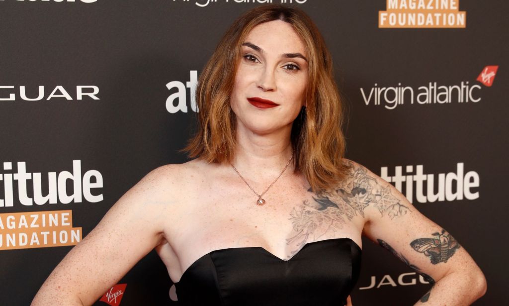 Trans author Juno Dawson wears a black dress with her hands on her hips