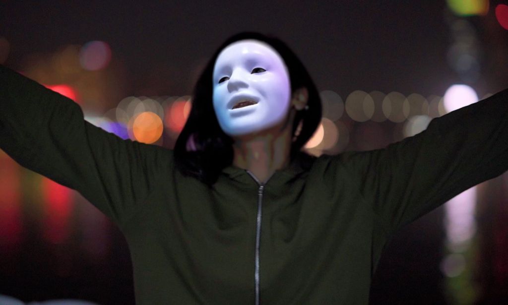 Laila, a trans person whose identity has been protected by masking technology, smiles and holds her arms out as she celebrates being able to escape LGBTQ+ persecution in Egypt