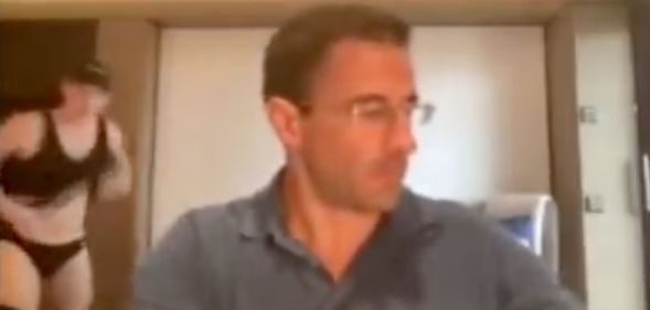 Dr Matt Heinz, a supervisor in Arizona, can be seen in the foreground in a screenshot from a Zoom call. In the background on the left hand side is a man wearing a swimsuit. He is in the process of taking off his shirt.