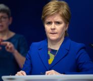 Scotland's first minister Nicola Sturgeon wears a blue and green top with a matching blue jacket during a press conference. She is standing at a podium