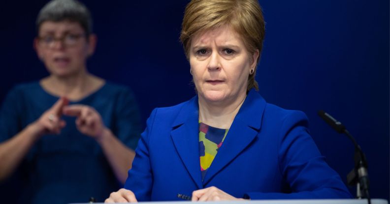 Scotland's first minister Nicola Sturgeon wears a blue and green top with a matching blue jacket during a press conference. She is standing at a podium