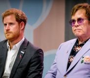 Prince Harry wears a white shirt and dark grey suit jacket as he sits next to Elton John, who is wearing a light purple jacket and dark shirt with floral patterning on it