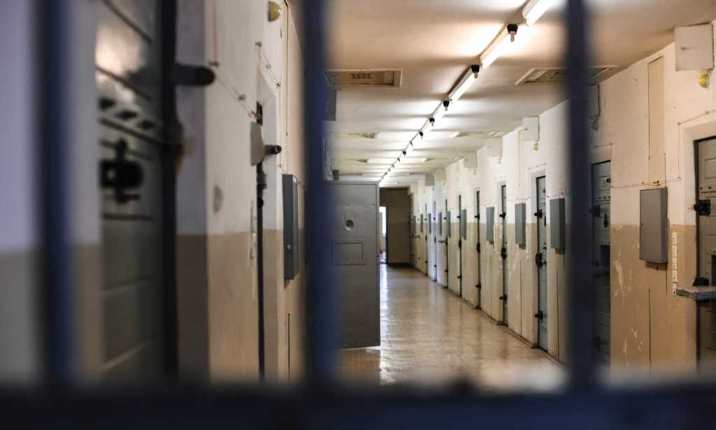 A photo of a prison corridor with prison bars shown clearly in the foreground