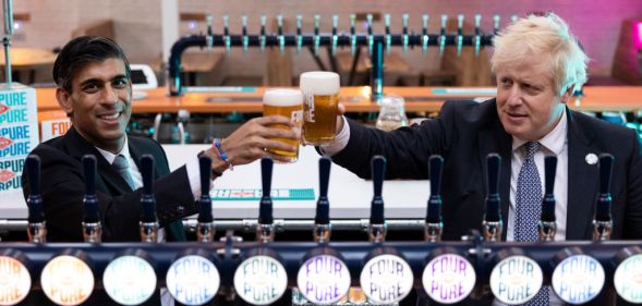 Boris Johnson and Rishi Sunak holding glasses on beer behind beer taps