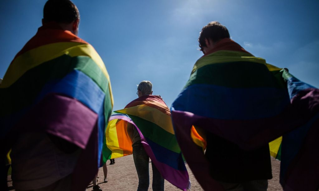 Three people wear rainbow LGBTQ+ Pride flags draped along their shoulders during a protest in Russia