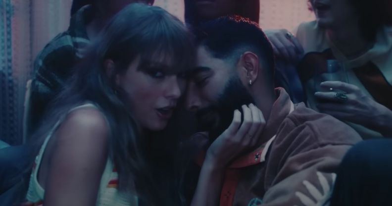 Taylor Swift looks towards the camera as she holds the face of Laith Ashley, a trans model and singer, in a house party scene in her "Lavender Haze" music video