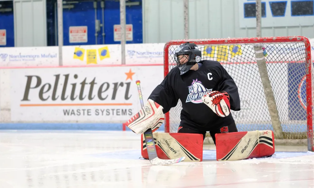 A Team Trans goalie poses in front of a goal while playing a hockey game