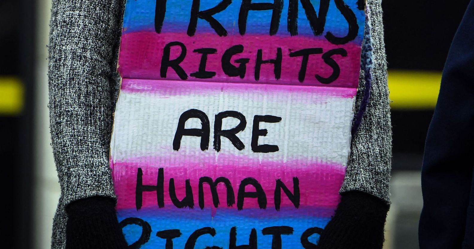 A person holds up a sign that reads 'Trans rights are human rights' in the colours of the trans pride flag