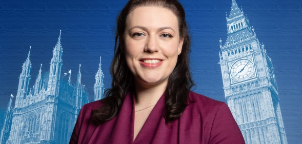 A publicity photo of Conservative MP Alicia Kearns wearing a purple suit and standing in front of a blue-tinted background with the Palace of Westminster projected onto it