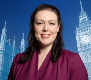 A publicity photo of Conservative MP Alicia Kearns wearing a purple suit and standing in front of a blue-tinted background with the Palace of Westminster projected onto it