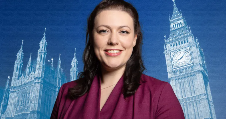 A publicity photo of Conservative MP Alicia Kearns wearing a purple suit and standing in front of a blue-tinted background with the Palace of Westminster projected onto it