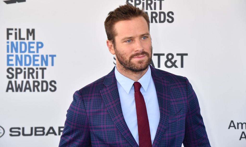 Armie Hammer stands infront of a red carpet screen during a photoshoot.