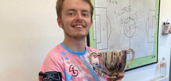 Arthur Webber holds up a trophy as he wears the TRUK United FC football kit, and he is set to captain the club's first all-trans men team