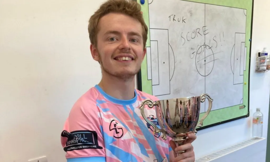 Arthur Webber holds up a trophy as he wears the TRUK United FC football kit, and he is set to captain the club's first all-trans men team