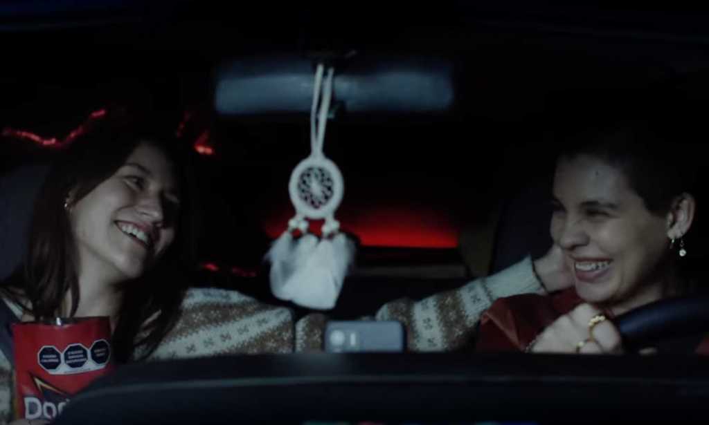 A screenshot from Doritos' 'Bold love' advert shows two women sitting next to each other in a car smiling with one woman touching the other's head.