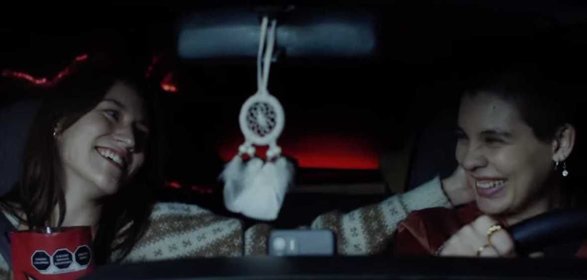 A screenshot from Doritos' 'Bold love' advert shows two women sitting next to each other in a car smiling with one woman touching the other's head.