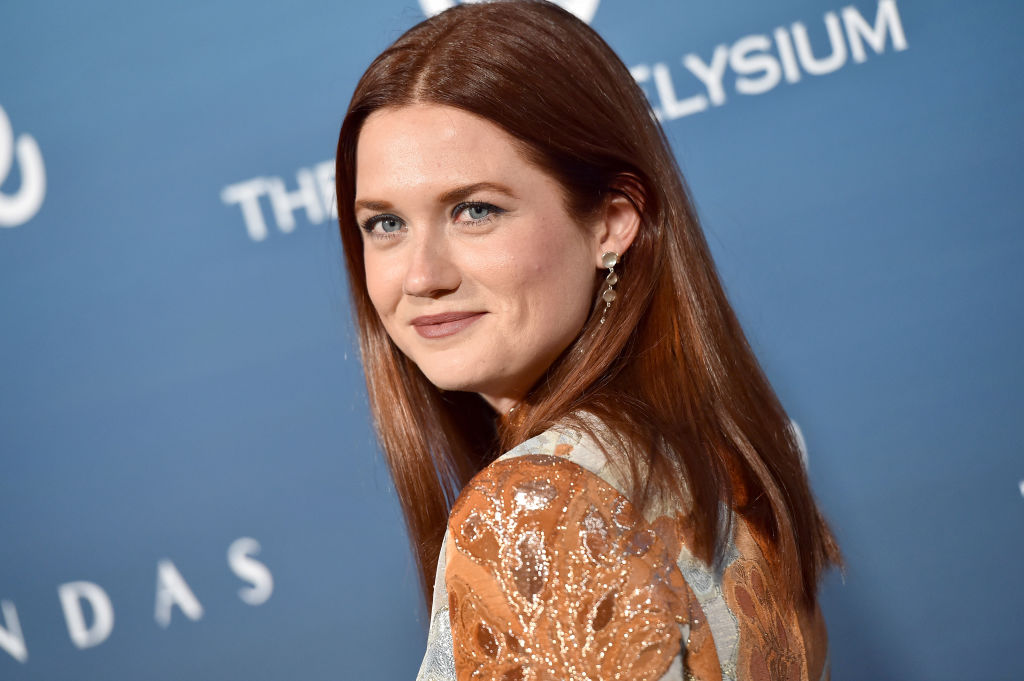 Harry Potter actor Bonnie Wright in an orange dress against a blue background