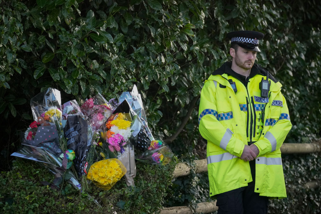 A police officer stands next to floral tributes at the entrance to Linear Park where 16-year-old Brianna Ghey was found with multiple stab wounds on a path in Culcheth on Saturday on February.