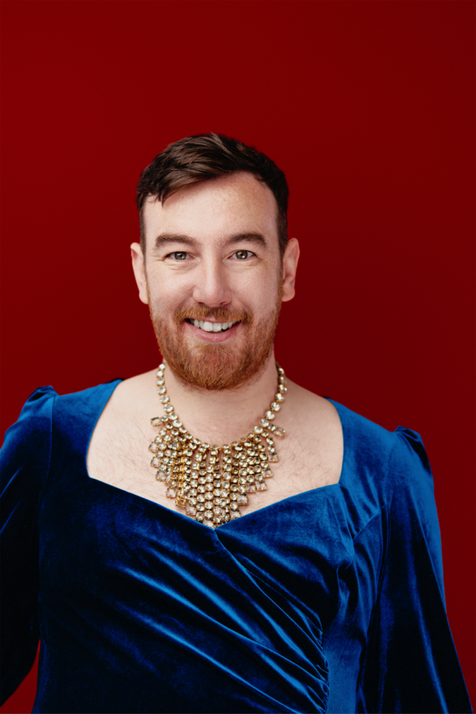 Chris King, wearing an ornate necklace and blue gown smiles at the camera.