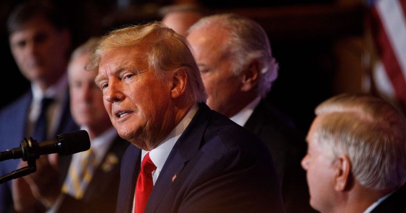 A photo shows Donald Trump wearing a navy suit, whit shirt and red tie speaking to an audience during a campaign speech.