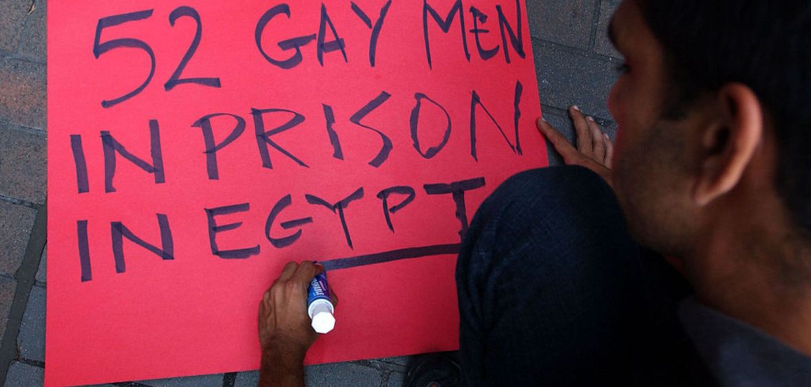 A person writes "52 Gay men in prison in Egypt" on a red sign for a protest in Egypt against the detention of LGBTQ+ people.