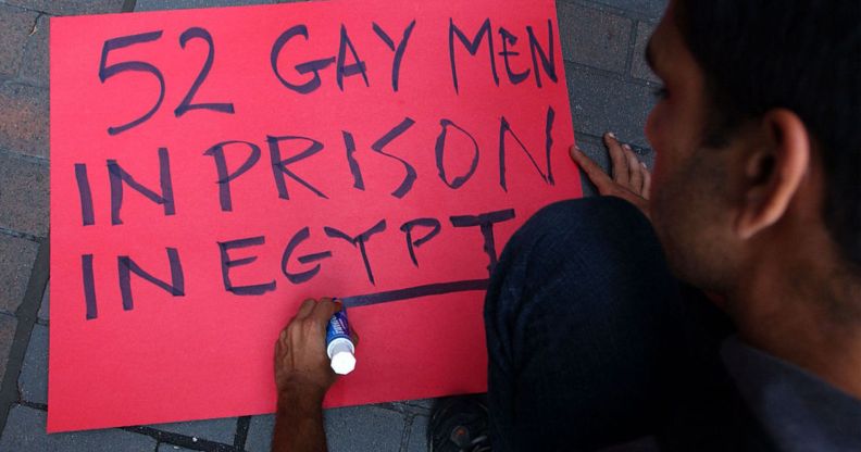 A person writes "52 Gay men in prison in Egypt" on a red sign for a protest in Egypt against the detention of LGBTQ+ people.