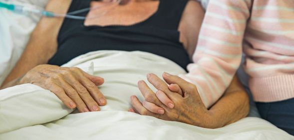 A bed-ridden person holds hands with a loved one.