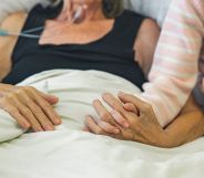 A bed-ridden person holds hands with a loved one.
