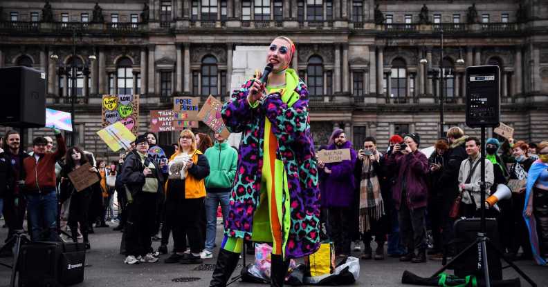 A photo from Glasgow's anti-trans rally shows someone from Cabaret Against The Hate Speech dressed in a brightly coloured clothes holding a microphone as they sing to the crowd