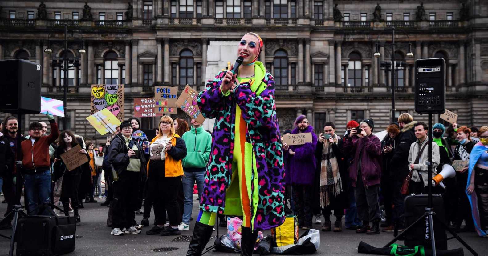 A photo from Glasgow's anti-trans rally shows someone from Cabaret Against The Hate Speech dressed in a brightly coloured clothes holding a microphone as they sing to the crowd