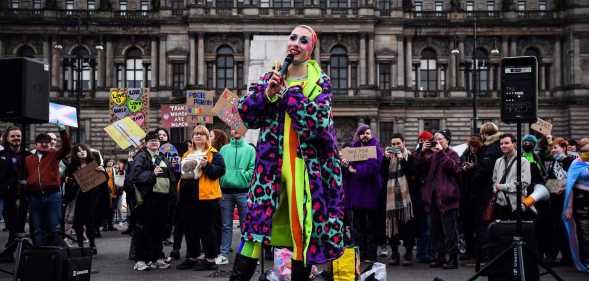 A photo from Glasgow's anti-trans rally shows someone from Cabaret Against The Hate Speech dressed in a brightly coloured clothes holding a microphone as they sing to the crowd