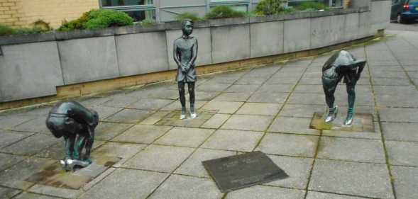 A photo shows the Gorbals Boys artwork piece in Glasgow. There are three statues showing three boys in different positions wearing women's shoes