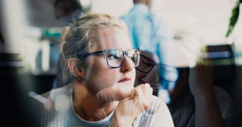 A woman with glasses is at work and is looking off towards a window.