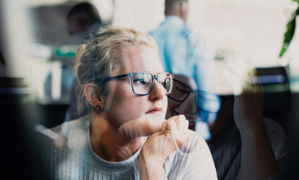 A woman with glasses is at work and is looking off towards a window.