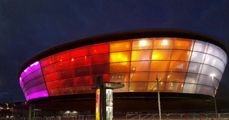 A photo showing the OVO Hydro Arena in Glasgow illuminated in lesbian Pride flag colours